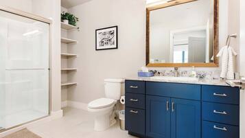 A modern bathroom with a glass shower enclosure, a white toilet, a blue vanity with drawers, and a large mirror.