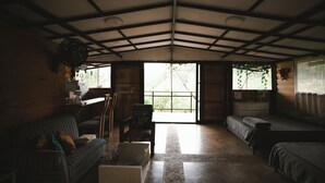 A cozy room with a sofa, a chair, a small table, and a bed. There are windows with curtains and a view of greenery outside. - San PEREGRINO (Manizales)