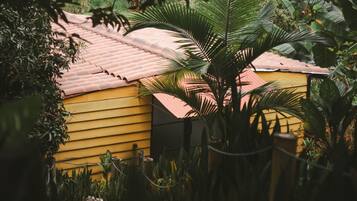 Un bâtiment jaune surmonté d’un toit rouge, entouré d’une végétation luxuriante et de plantes.