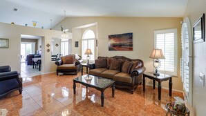 A spacious living room with a large sofa, a coffee table, and a dining area in the background.