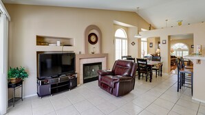 A living room with a flat-screen TV, leather recliner, fireplace, dining area, and kitchen.