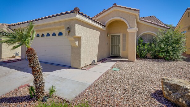 A residential house with a beige facade, a tiled roof, and a gravel driveway.