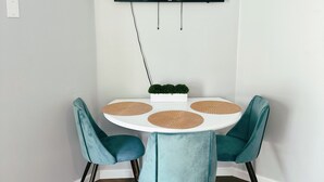 A dining area with a round table, teal chairs, a flat-screen TV mounted on the wall, and a small potted plant on the table. - Bikes, Beaches and Quaint Floridian Downtowns (Palm Harbor)