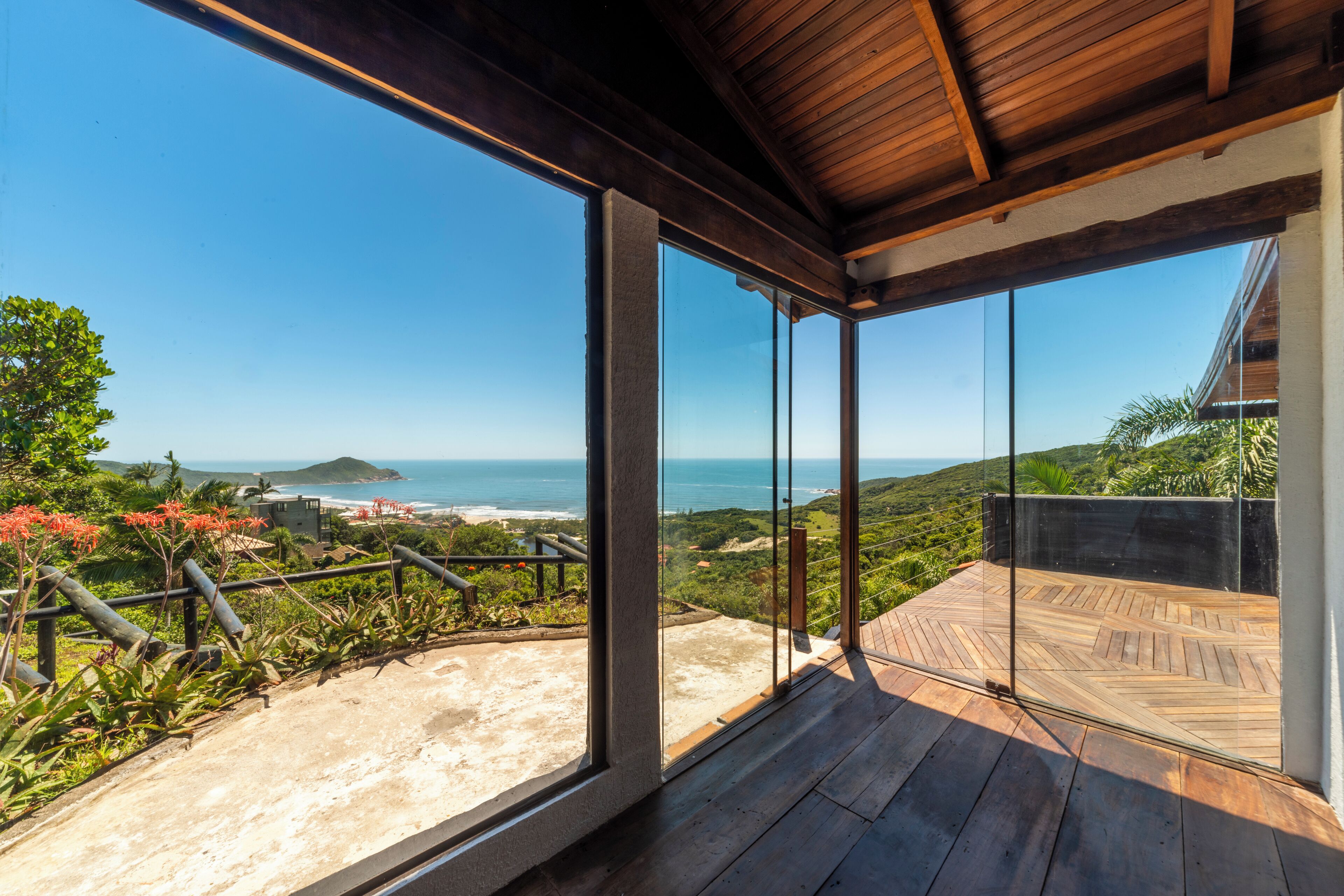 A modern balcony with glass doors, offering a view of the ocean and hills.