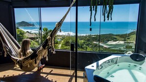 A hammock chair on a balcony overlooking a beach, a hot tub, and a view of the ocean and landscape. - Pousada Villa Buena Vista (Imbituba)