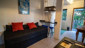 A living room with a black sofa, red cushions, a coffee table with remote controls, and a bar area with stools. - Pousada Villa Buena Vista (Imbituba)