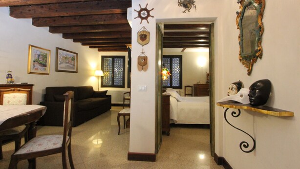 Una sala de estar acogedora con techo de madera, una mesa de comedor con sillas, un sofá y una cama con mesita de noche.