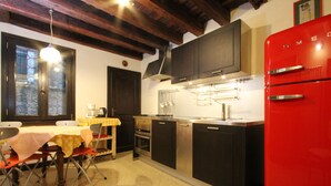Cocina compacta con armarios oscuros, un refrigerador rojo y una zona de comedor con mesa y sillas.