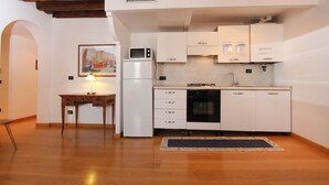 A compact kitchen with white cabinets, a microwave, a refrigerator, and a stove. There's a small table with a lamp and a rug on the floor. - Apartment Moro 5 (80mt. from Rialto´s Bridge) (Venecia)