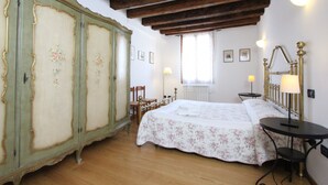A bedroom with a bed, wooden floor, a large wardrobe, a small table, and a window with curtains. - Apartment Moro 5 (80mt. from Rialto´s Bridge) (Venecia)