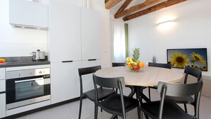 Cuina moderna amb armaris blancs, forn integrat i taula rodona de fusta amb caires.