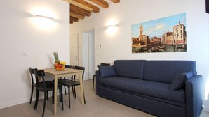A room with a wooden ceiling, a blue sofa, a dining table with chairs, and a painting of a cityscape on the wall. - Apt. Canaletto (Residence Artisti) (Venecia)
