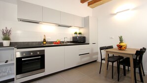 A modern kitchen with white cabinets, a built-in oven, a microwave, and a dining table with chairs. - Apt. Canaletto (Residence Artisti) (Venecia)