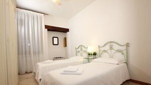 Une chambre d’hôtel avec deux lits, une table de chevet avec une lampe, un miroir au mur et une fenêtre avec des rideaux.