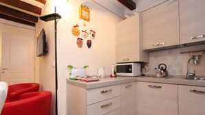 Eine Küche mit Mikrowelle, Spüle und Schränken. An der Wand befinden sich dekorative Gegenstände und ein roter Stuhl.
