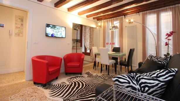 Ein Wohnzimmer mit einem zebra-gemusterten Teppich, einem roten Sessel, einem schwarzen Sofa und einem Essbereich mit Tisch und Stühlen.