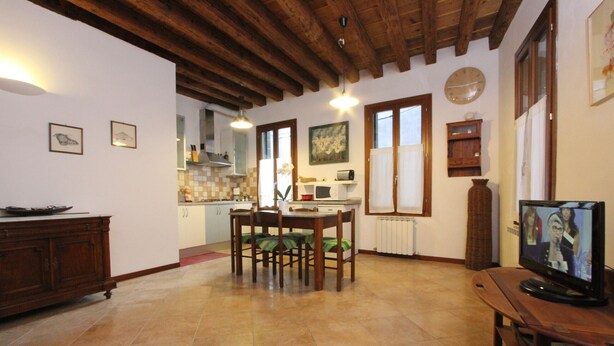 A spacious living area with a wooden dining table, chairs, a television, and a kitchen in the background. - Apartment Laura (near Biennale Arsenale) (Venecia)
