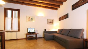 A living room with a sectional sofa, a television on a wooden stand, a radiator, and framed pictures on the wall. - Apartment Laura (near Biennale Arsenale) (Venecia)