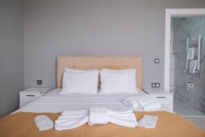 A neatly made bed with white linens, two pillows, and a folded towel on a brown bedspread. There are two bedside tables with lamps, a marble-patterned wall, and a door to the right. - MY HOME IN TRABZON (Trabzon)