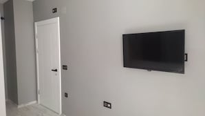 En hall med en vit dörr, en väggmonterad platt-TV och en ljusgrå vägg.