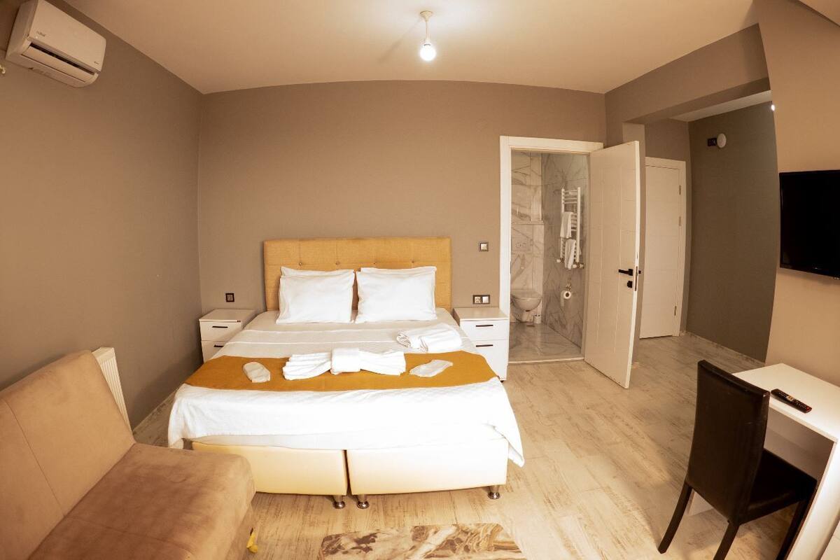 A hotel room with a bed, a desk, a chair, an air conditioner, and a TV.