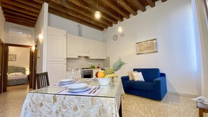 A dining area with a glass table set for four, white cabinets, a blue sofa, and a kitchen in the background. - Apartment Canova Canal View (Venecia)
