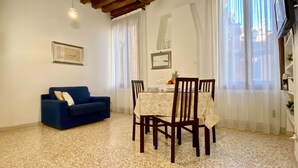 A dining area with a table set for two, a blue sofa, and a chandelier. - Apartment Canova Canal View (Venecia)