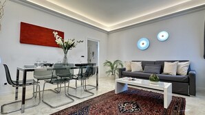Un salon moderne comprenant un coin repas, un canapé gris, une table basse et un tableau abstrait rouge.