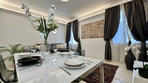 Un coin repas avec une table dressée pour quatre personnes, un vase rempli de fleurs blanches, une œuvre d’art représentant une carte accrochée au mur et une vue sur l’extérieur par la fenêtre.