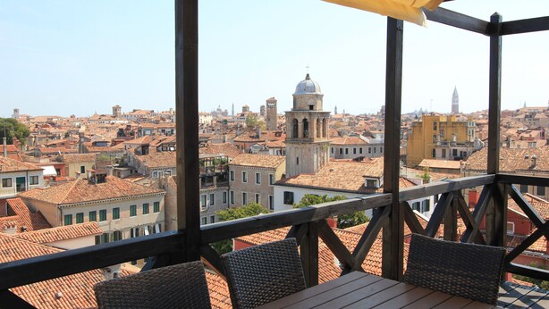 A terrace with wicker furniture and a view of a cityscape with historic buildings and a prominent tower. - Apartment Altana, Amazing Grand Canal View (Venecia)