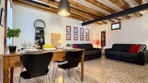 A dining area with a wooden table, black chairs, and a black sofa. There is a mirror on the wall, framed pictures, and a plant on the table. - San Giovanni (Venice Historical Centre) (Venecia)
