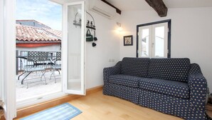 Un salon chaleureux avec un canapé, une table à manger et des chaises, et une vue sur un toit recouvert de tuiles rouges.