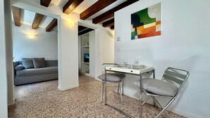 A modern interior with a dining area featuring a table and two chairs, a grey sofa, and a colorful abstract painting on the wall.