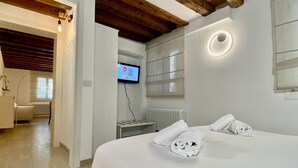 Habitació d'hotel moderna amb un llit gran, televisió penjada a la paret i una finestra amb persianes.