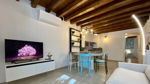 Un saló modern amb televisió de pantalla plana, zona de menjador amb taula i cadires, i cuina al fons.