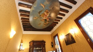Um quarto com teto abobadado, vigas de madeira, uma moldura decorativa no teto, arandelas, um armário de madeira e uma janela com vitrais.