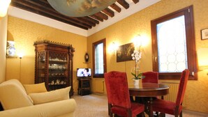 Uma sala de estar com sofá, mesa de jantar com cadeiras, aparador de madeira, televisão e janela com vista.