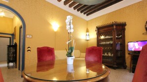Uma área de refeições com uma mesa de vidro, cadeiras vermelhas, uma planta em vaso, um armário de madeira e uma televisão.