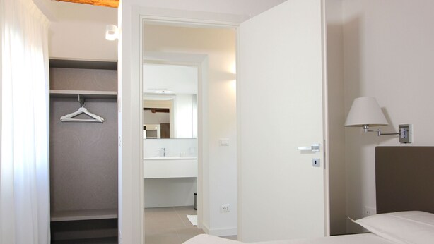 Habitación de hotel con cama, armario y baño visible a través de una puerta abierta.