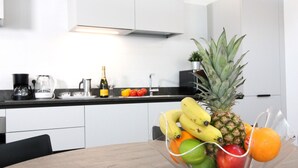 Una cocina moderna con armarios blancos, encimera negra y un frutero con plátanos, piña, manzana y naranja.