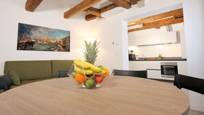 Un comedor con una mesa redonda, un frutero, un sofá verde y una cocina al fondo.