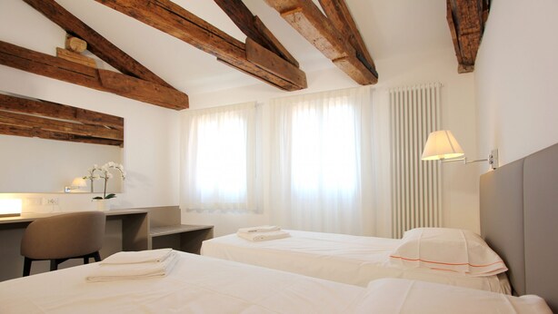 Habitación de hotel con dos camas, un escritorio, una silla y una lámpara.