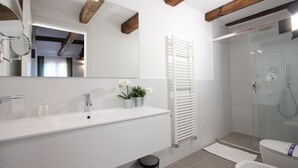 Un baño moderno con lavamanos blanco, espejo y cabina de ducha con paredes de vidrio.