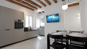 Een moderne keuken met inbouwapparatuur, een eethoek met een tafel voor vier personen en een aan de muur bevestigde televisie.