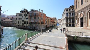 A canal with buildings on either side, a bridge, and people walking.