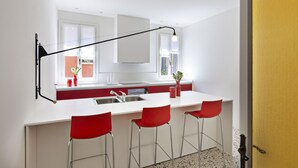 A modern kitchen with a white countertop, red bar stools, a black pendant light, and a window with a view.