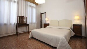 Une chambre d’hôtel avec un grand lit, une table de chevet en bois, une petite table d’appoint, un miroir et une lampe.