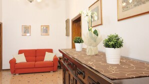 Une pièce avec un canapé rouge, un meuble en bois, deux plantes en pot et des tableaux encadrés accrochés au mur.