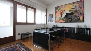 Een moderne keuken met een groot kookeiland, zwarte stoelen, een eettafel en een boekenplank vol boeken en decoratieve spullen.