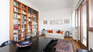 Een kamer met een eettafel, stoelen, een boekenkast, een bank en een kamerbreed tapijt.